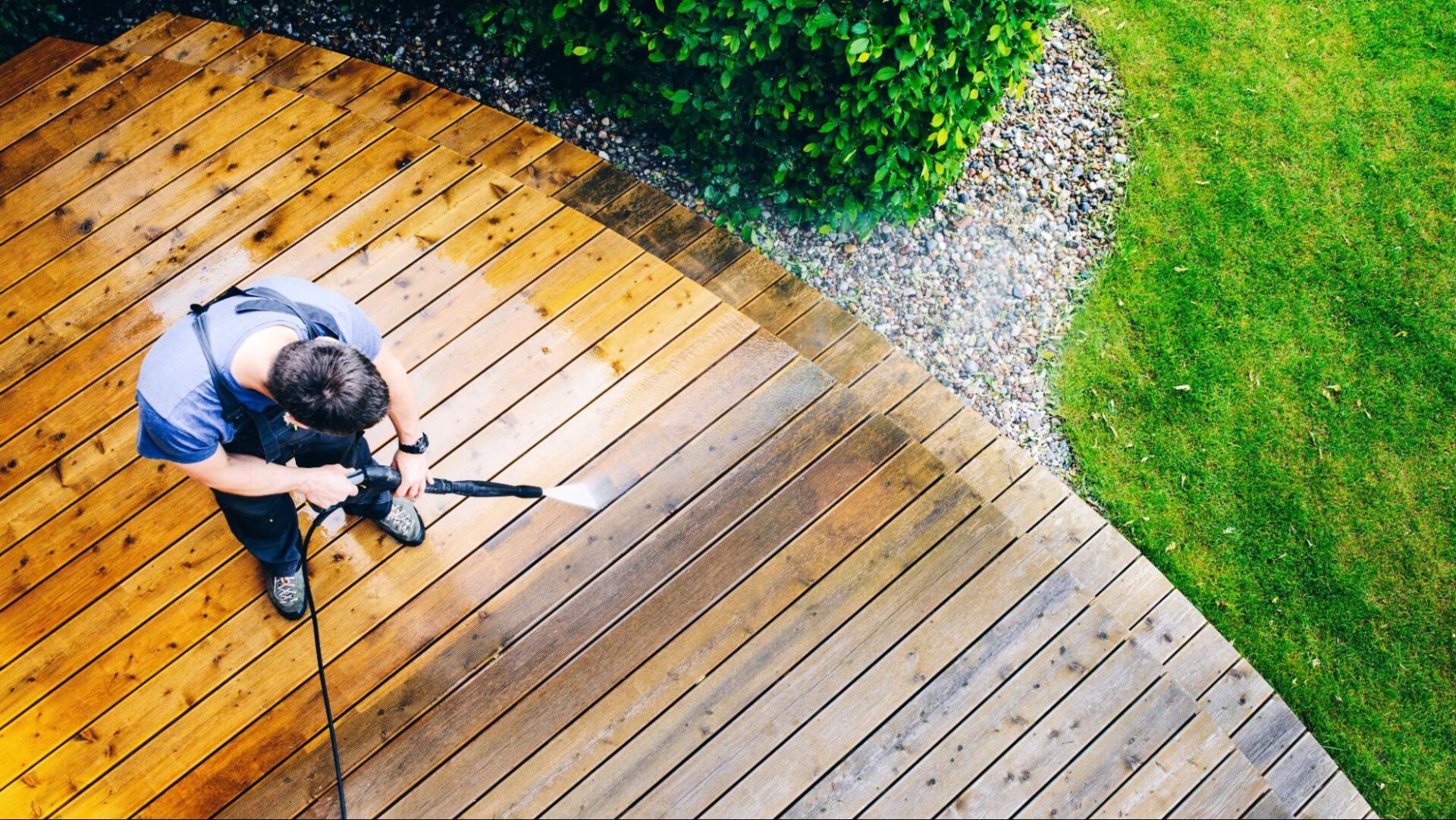 Patio & Deck Cleaning Person power washing a wooden deck, contrasting the cleaned area with the dirty surface.