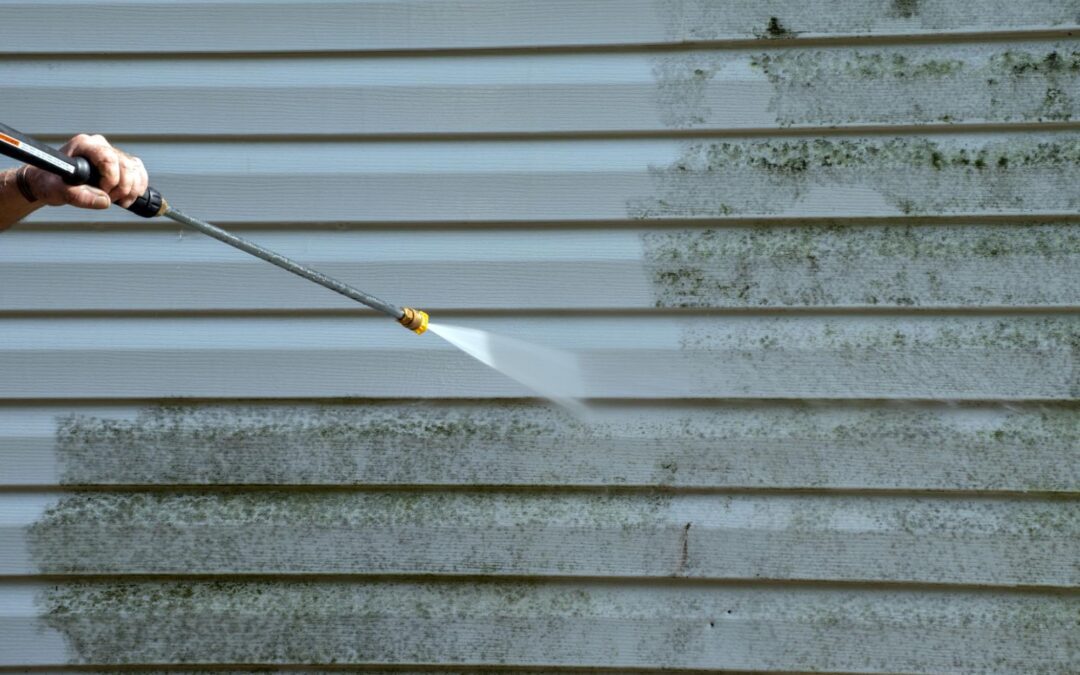 Pressure washing a dirty siding, with a clear water spray visible.
